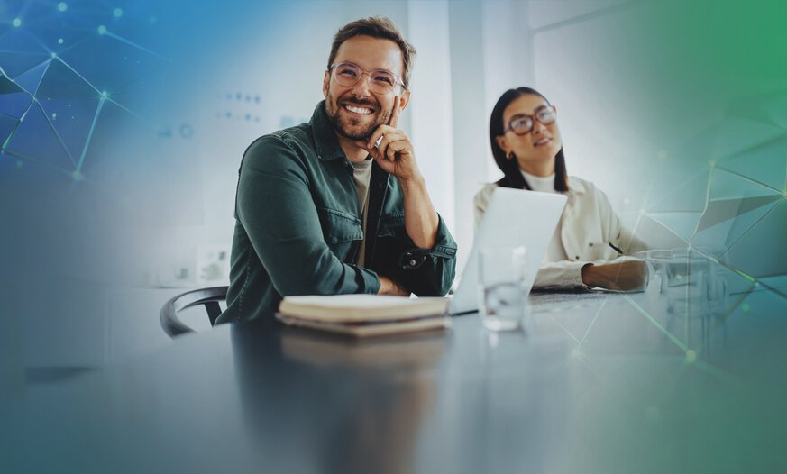 Mann und Frau sitzen an einem Schreibtisch in einer Bürosituation an Laptops